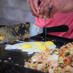 Cracking an egg to cook on the flat-top grill before mixing it in with the rest of the fried rice.