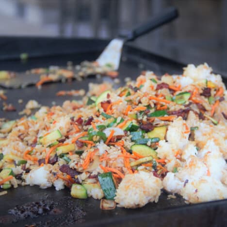Looking across a flat top grill with a pile of fried rice with plenty of veggies.
