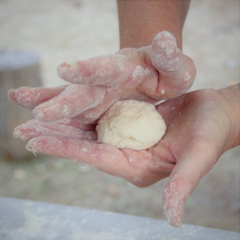 A person rolling a ball of dough in their hands.