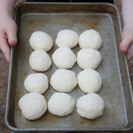 A batch of dough balls sits on a baking tray.