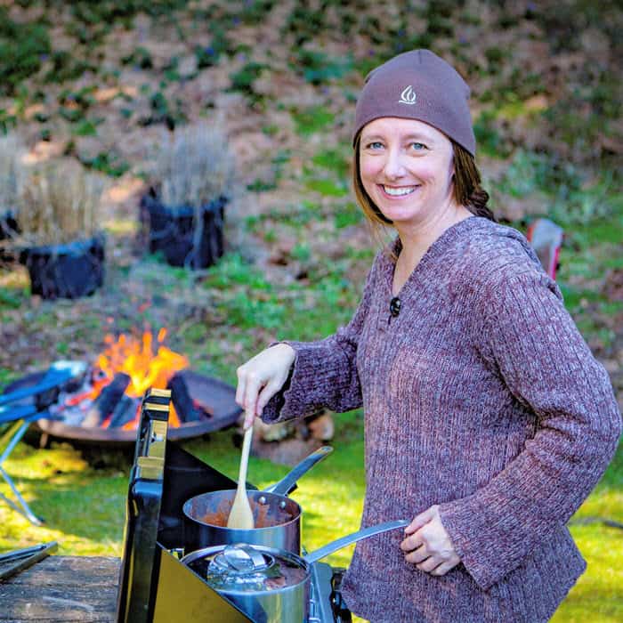 Portrait Photo of Saffron Hodgson cooking on a Camp Stove with a campfire in the background