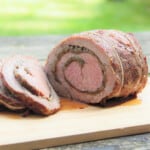A smoked sage and onion beef roulade, with a few slices taken from it, and resting on a wooden cutting board.
