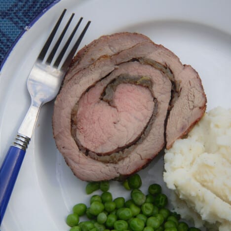 A single slice of the sage and onion roulade, showing the swirl, sitting on a white plate with peas and mashed potatoes.