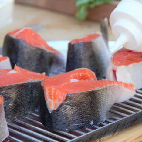 Raw pieces of skin-on salmon sitting on a grill grate on a wooden cutting board.