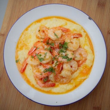 Looking down into a white camping bowl with shrimp and grits on a wooden cutting board.