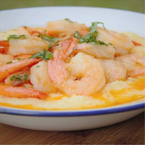 Looking into a white camping bowl of shrimp resting on cheesy grits.