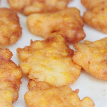Cooked corn fritters resting on a white paper towel.