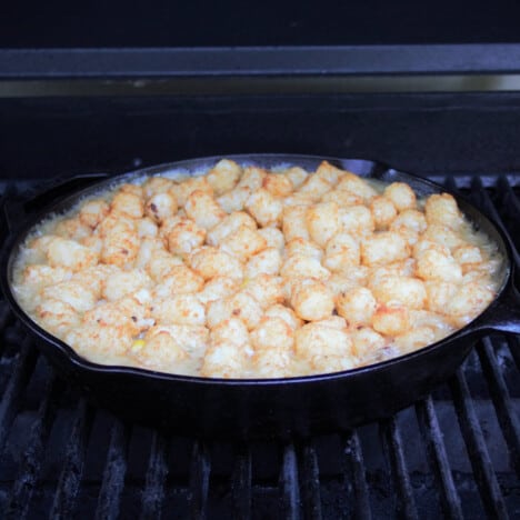 A cast iron skillet with tater tots on top of the filling, sitting in an enclosed barbecue.