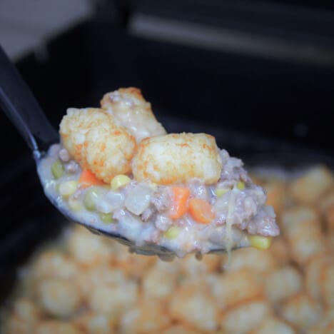 A spoonful of the tater tot casserole is being held above the dish, with the filling prominent.
