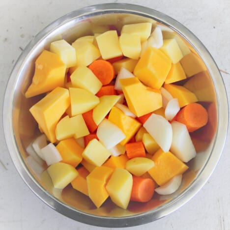 Aerial view of a stainless steel bowl filled with chopped butternut squash (pumpkin), carrots, potatoes, and onions.