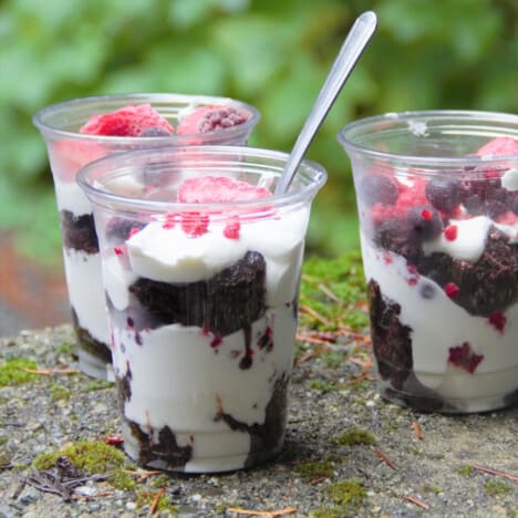 Three plastic cups layered with cream and chocolate brownie then topped with berries.
