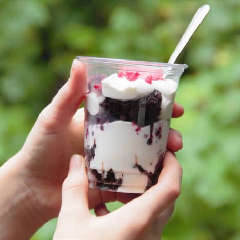 A single cup of parfait being held up to show the chocolate brownie and cream layers.