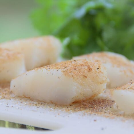 Individual portions of white fish sprinkled with salt and spices resting on a cutting board.