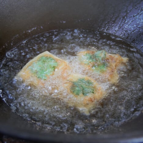 Three packets of wrapped fish and cilantro leaves are frying in bubbling hot oil, the rice paper turning golden brown.