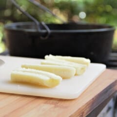Quartered fresh bananas sitting on a chopping board in front of a Dutch oven.