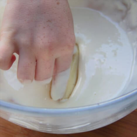 A banana being hand-dipped into the prepared batter.