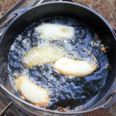 Four banana fritters cooking in an oil-filled Dutch oven.