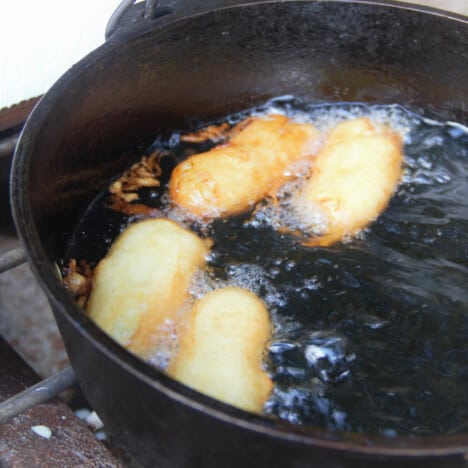 Four golden brown banana quarters deep frying in a Dutch oven.