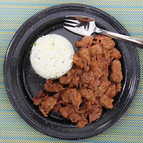 Looking down on a black camp plate with a serving of beef Rendang and steamed rice.