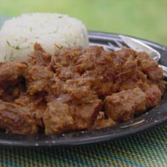Looking into a serving of Rendang curry with a serving of white rice on a black camping plate.