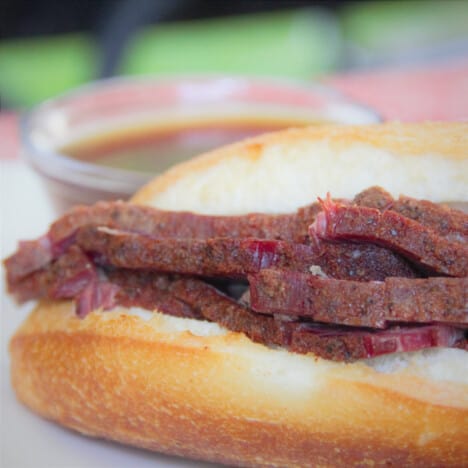 Close look at the brisket slices in a roll with the au jus in the background.