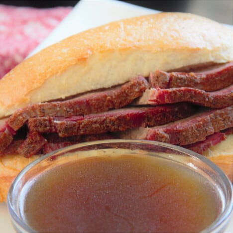 A small bowl of barbecue smoked brisket au jus in front of a brisket roll.