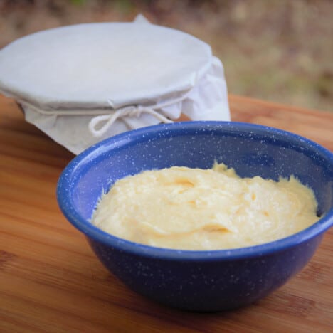 A blue camp bowl is filled with the pudding mixture with a completed pudding wrapped in baking paper and string applied in the background.