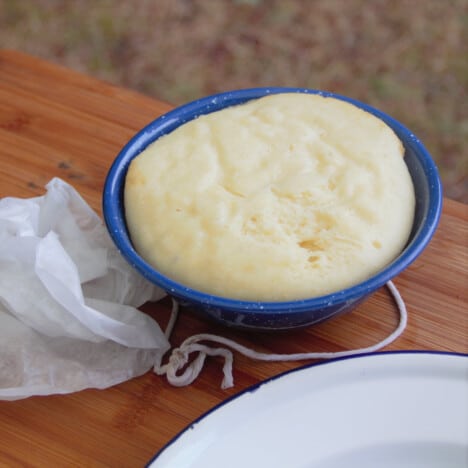 A cooked steamed pudding sits in a camp bowl, with a plate next to it, waiting to be inverted.