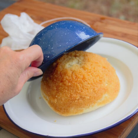 A steamed pudding is being tipped out of a blue camping bowl onto a white serving plate.