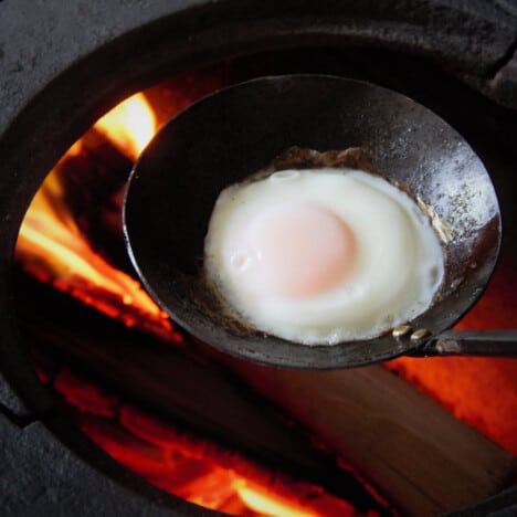 A cooked egg sits in a ladle over a hot fire.