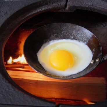 A raw egg sits in a ladle over a hot fire.