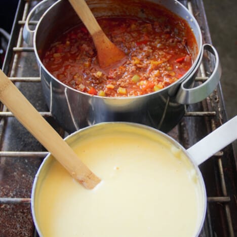 The two sauces, béchamel and bolognese, are being cooked on a camp gas stove.
