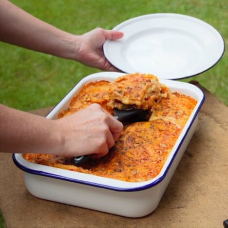 The first slice of lasagne being served from the baking dish of finished lasagna.