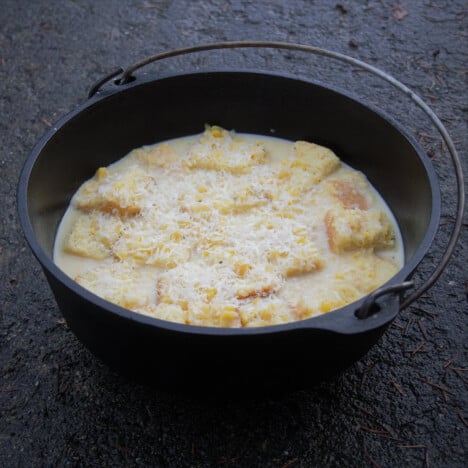 A Dutch oven containing corn pudding mix, chunky with bread cubes and ready to cook.