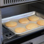 Six cream cheese cookies are baking on a sheet pan in a camping oven.