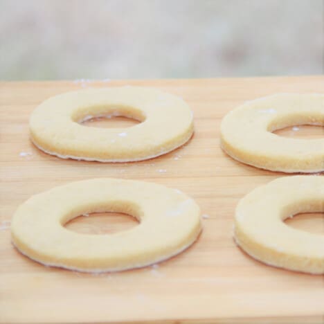 Four raw donuts sit on a chopping board.