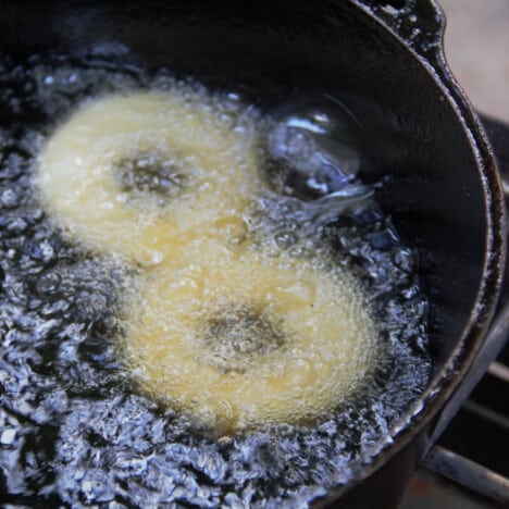 Two donuts deep frying in oil in a Dutch oven.