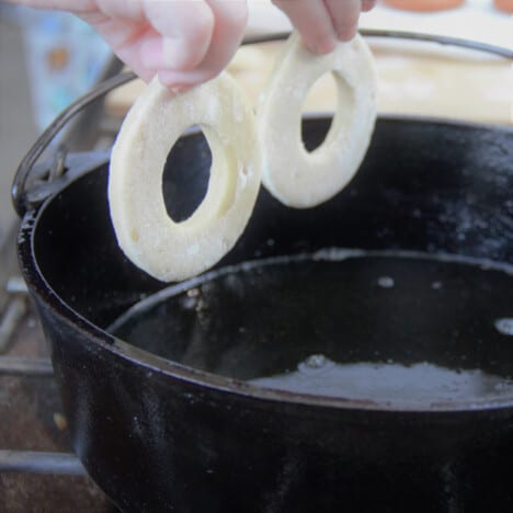 Two donut shaped pieces of dough being placed into oil in a Dutch oven.