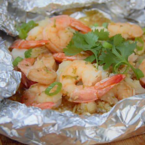 Cooked shrimp in it foil packet garnished with spring onion and cilantro.