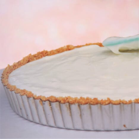 A spatula is smoothing the top of the lemon cheesecake filling in a pie tin.