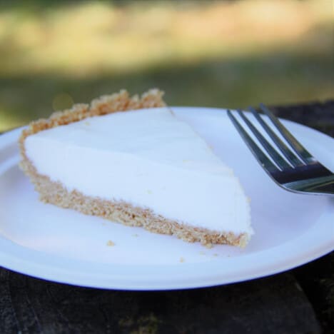 A single slice of lemon cheesecake sits on a white plate with a fork.