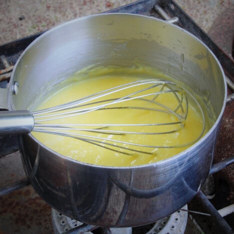 A whisk resting in a saucepan of lemon curd sitting on a camp stove.