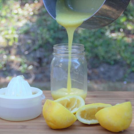 Fresh lemon curd being poured from a saucepan to a jar.