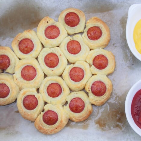 A batch of Hot Dog Bites being served on the tray they were cooked on along with a bowl of ketchup and mustard for dipping.