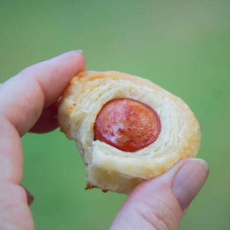 Holding up a single cooked hot dog bite.