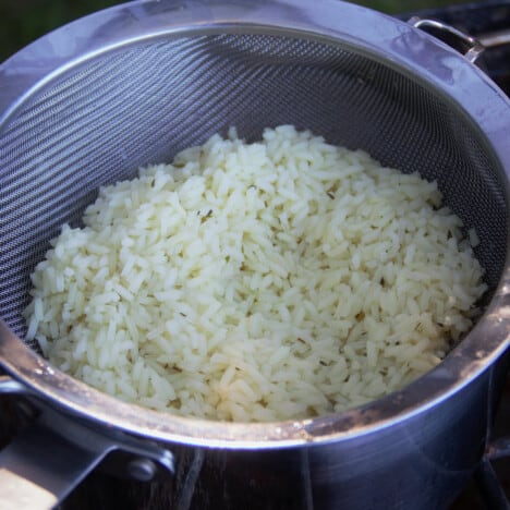 Cooked rice draining in a sieve over a pot.