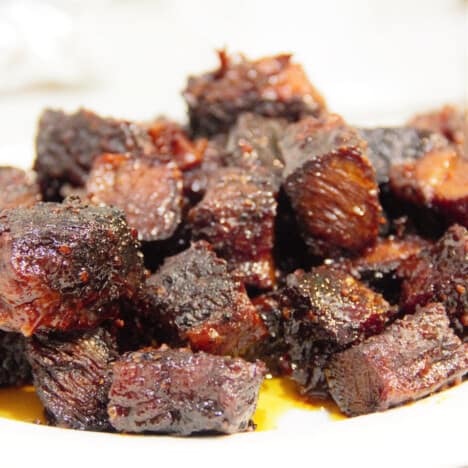 A pile of smoked short beef rib cubs, with glaze, sit on a white plate.