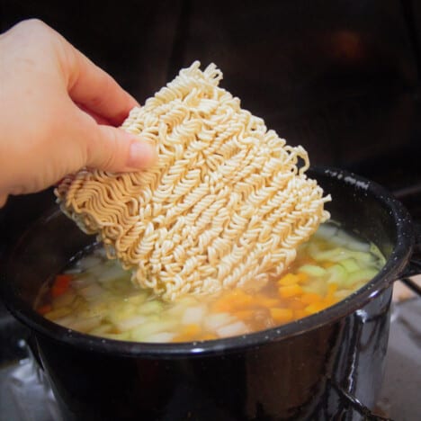 A bock of ramen noodles being added to the turkey soup cooking on a gas camp gas stove.