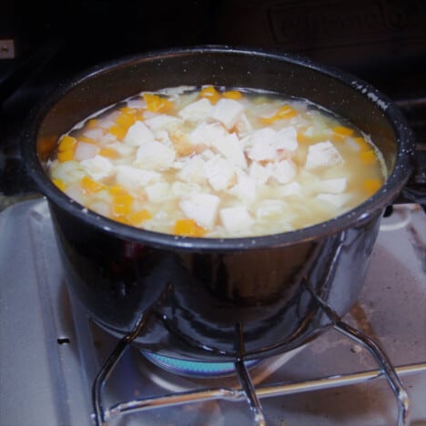 A black pot cooking turkey noodle soup on a camp gas stove.