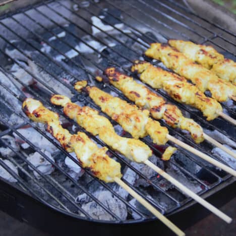 Looking down onto a grill with briquettes while chicken satay skewers cook.